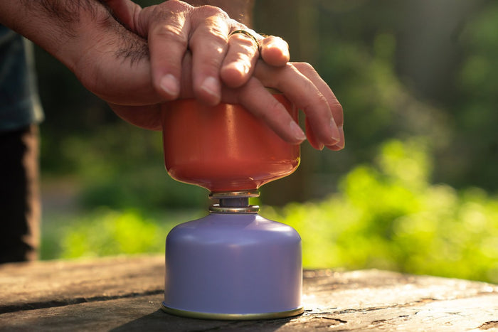 AlpenFlow Fuel Transfer Valve connecting two fuel canisters, hand pressing down outdoors