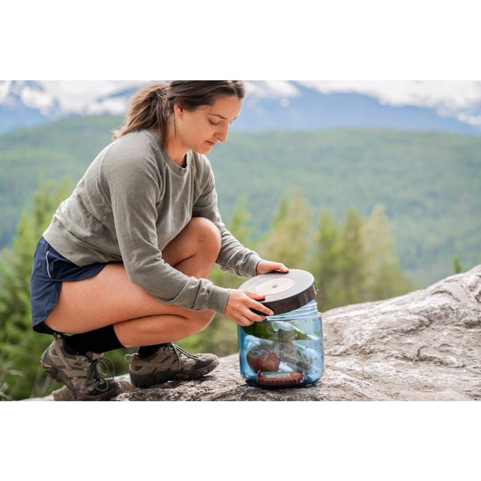 BearVault BV450-Jaunt canister being packed by a hiker, mountains behind