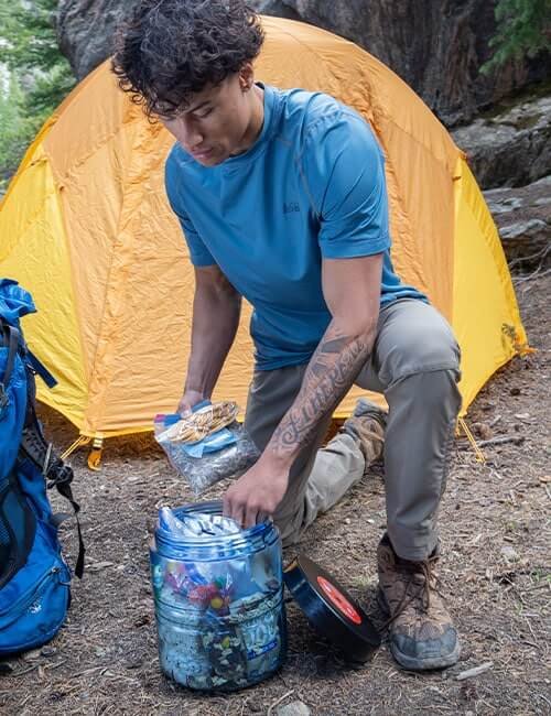 BearVault BV475-Trek canister being packed beside a tent on the trail