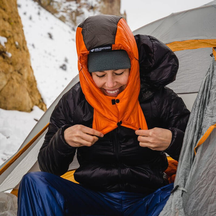 Enlightened Equipment Torrid Hood worn by a person at a snowy campsite, orange lining