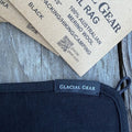 Glacial Gear Trail Rag Elite in black, corner detail with woven label and merino wool hang tag