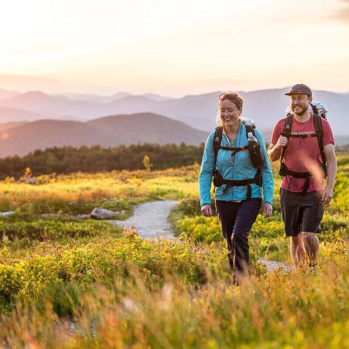 Hyperlite Mountain Gear Bottle Pocket – two hikers walking a meadow trail at sunset, bottles in the pockets