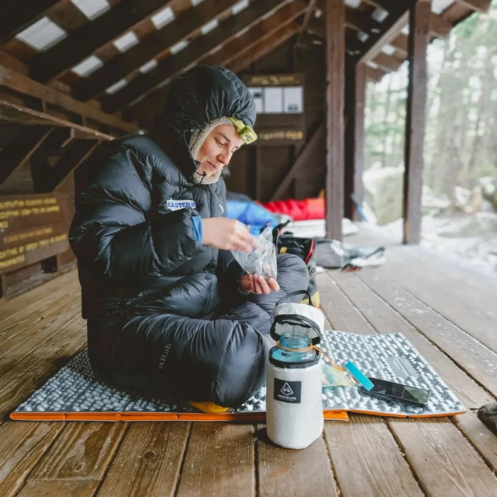 Hyperlite Mountain Gear Insulator on a sleeping pad beside a hiker eating in a shelter