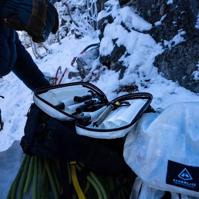 Hyperlite Mountain Gear Prism Ice Screw Case open with ice screws, resting on rope beside an icy climb