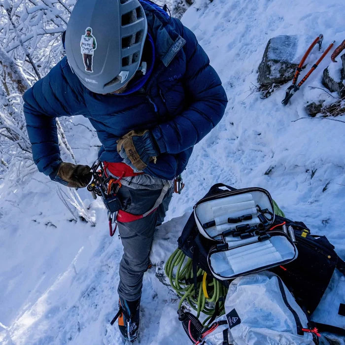 Hyperlite Mountain Gear Prism Ice Screw Case – climber racking gear beside the open case on snow