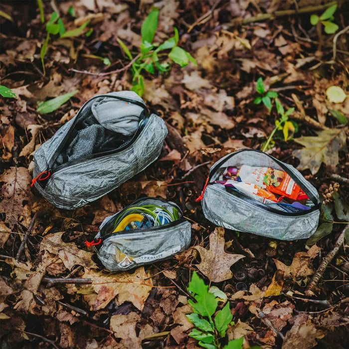 Hyperlite Mountain Gear Zippy pouches in three sizes, open and packed with gear on a forest floor