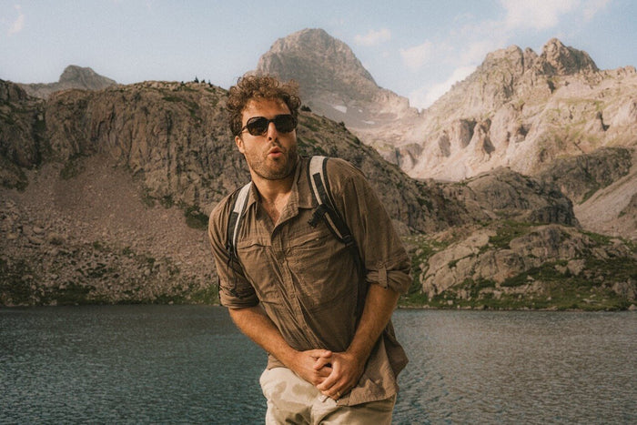 Ombraz Cammina armless sunglasses worn by a hiker standing beside an alpine lake