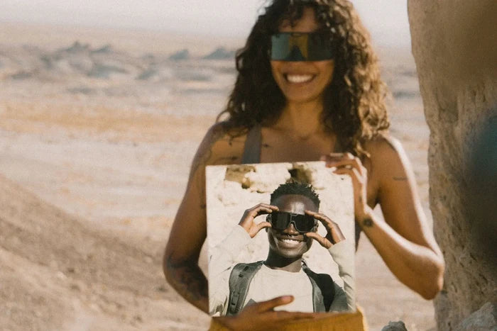 Ombraz Refugio armless sunglasses worn by a woman holding a mirror with a reflection