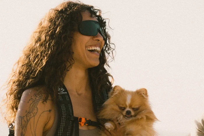 Ombraz Refugio armless sunglasses worn by a laughing woman holding a small dog