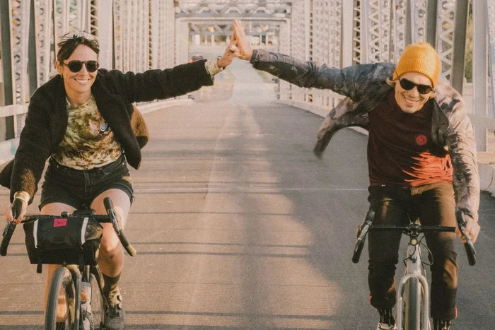 Ombraz Viale armless sunglasses, tortoise frame with grey lenses – worn by two cyclists high-fiving on a bridge