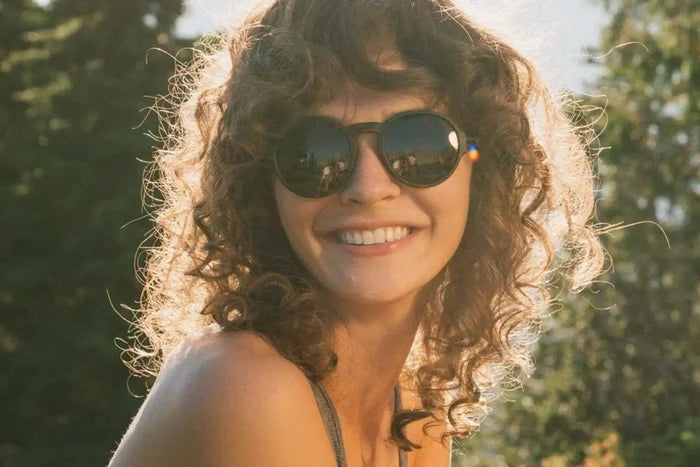 Ombraz Viale armless sunglasses, tortoise frame with grey lenses – worn by a smiling woman with curly hair outdoors