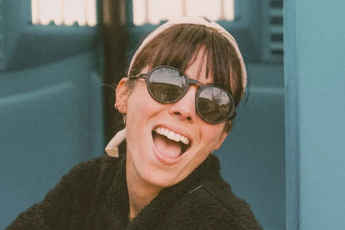 Ombraz Viale armless sunglasses, tortoise frame with grey lenses – worn by a laughing woman against a teal wall