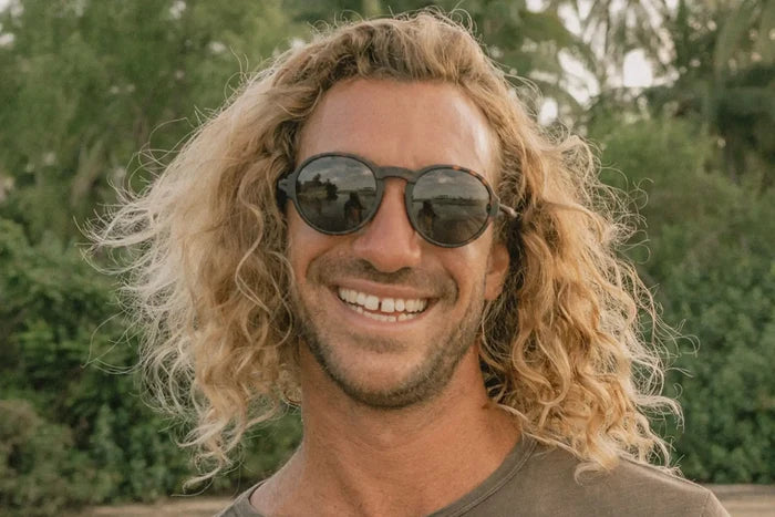 Ombraz Viale armless sunglasses, tortoise frame with grey lenses – worn by a smiling man with long curly hair