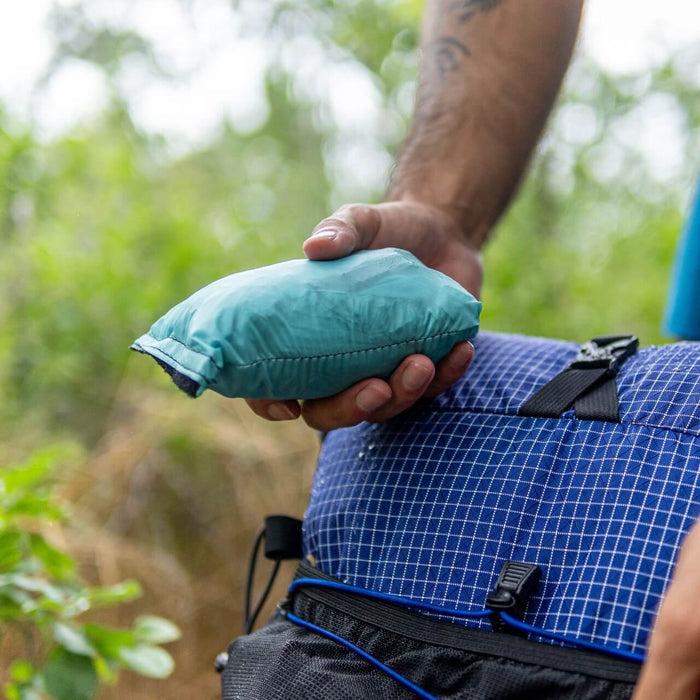 ULA Pack Cover in teal folded into a palm-sized bundle, held over a blue pack